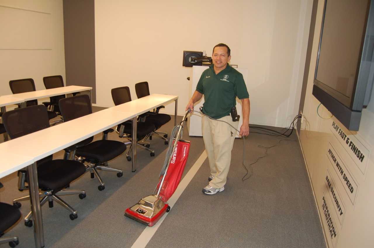 A man is vacuuming the floor in an office.